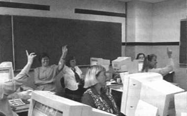 [ Billede: Elever sidder med fingren oppe i klasseværelset ]