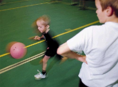 [Billede: Dette billede er taget i en gymnastiksal. Man ser en lille dreng løbe forbi med en bold. Ved siden af står der en voksen, og kigger på.]